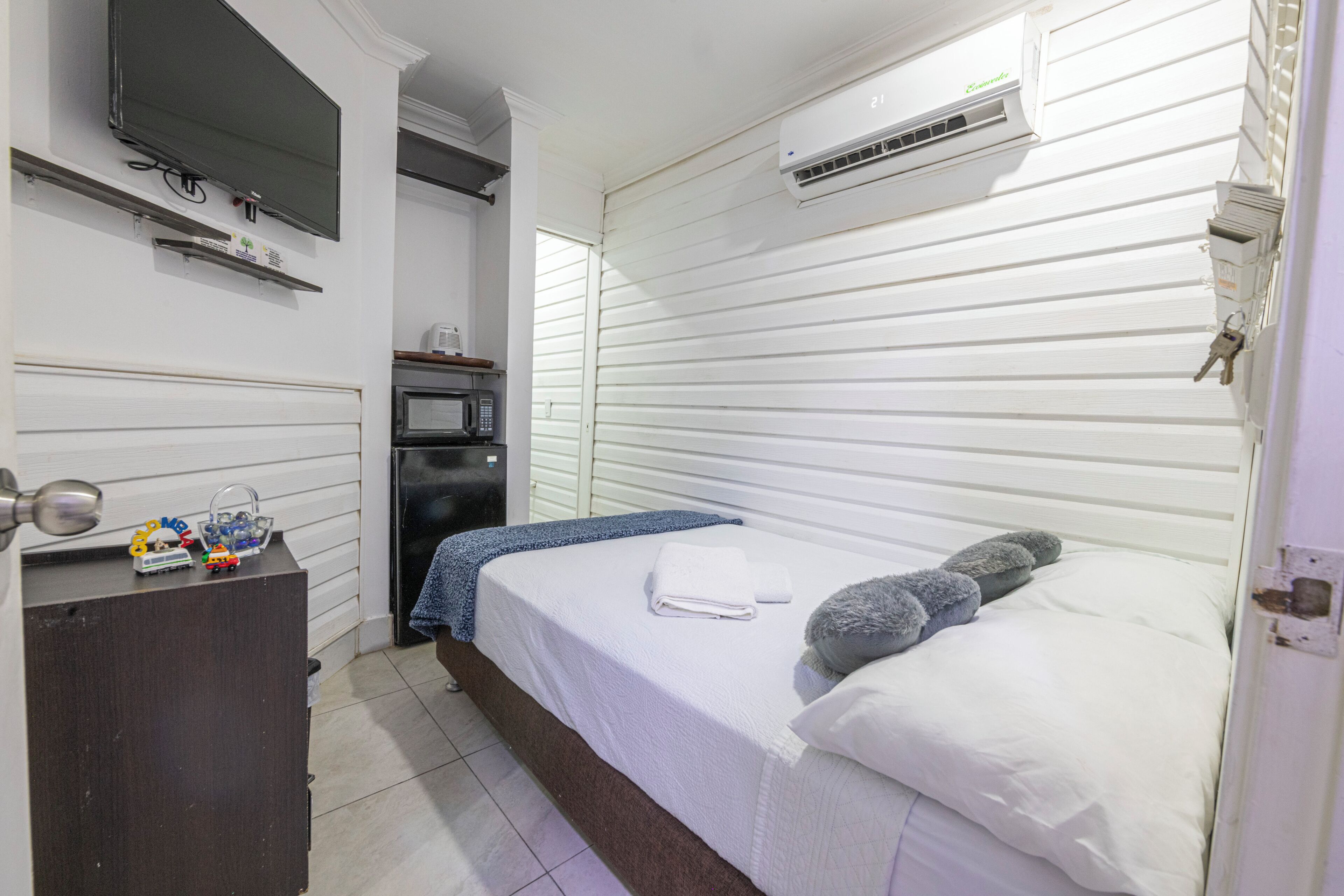 A bedroom with a bed, a television, an air conditioner, a microwave, and a small desk with toys.