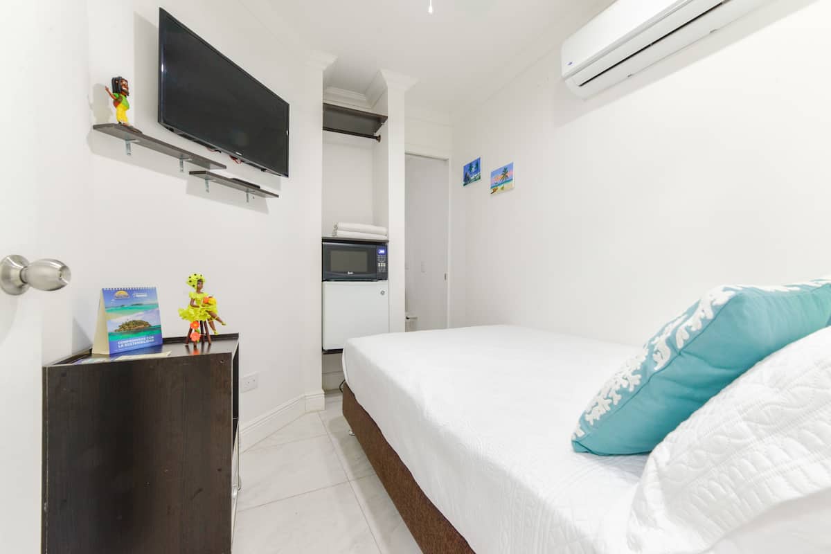 A hotel room with a bed, a TV mounted on the wall, a microwave, and a small desk with a book and figurine.