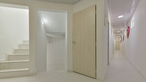 Un pasillo con paredes blancas, una puerta de madera y una escalera que sube a un nivel superior.