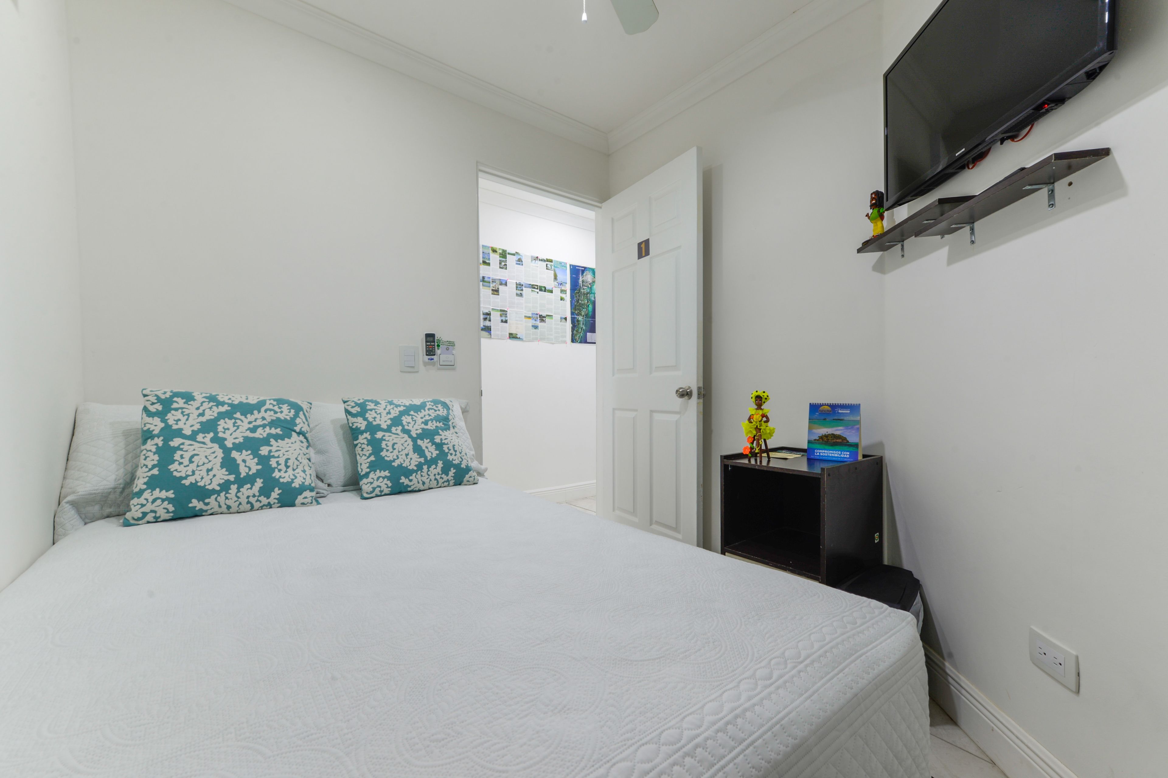 A bedroom with a bed, a TV mounted on the wall, and a door leading to another room.