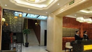 A hotel lobby with a reception desk, seating area, and a staircase leading to another floor. - Banfu Hotel (Harbin)