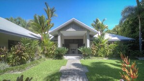A house with a symmetrical facade, a central entrance, and a well-maintained lawn with tropical plants. - Tranquility By The Course Port Douglas (Craiglie)