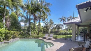 A swimming pool with lounge chairs, surrounded by palm trees and a covered patio area. - Tranquility By The Course Port Douglas (Craiglie)