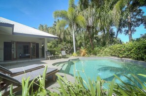 A pool area with lounge chairs, a covered patio, and tropical vegetation.