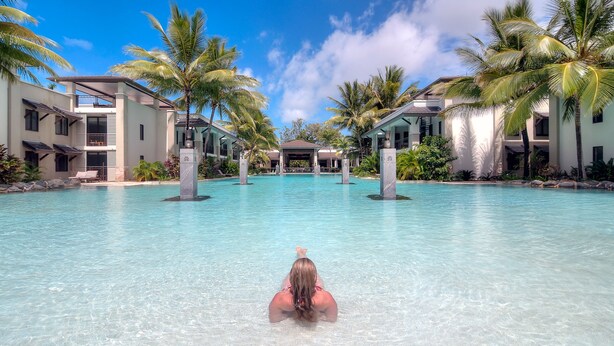 Piscina de resort con agua cristalina, rodeada de palmeras y edificios modernos.