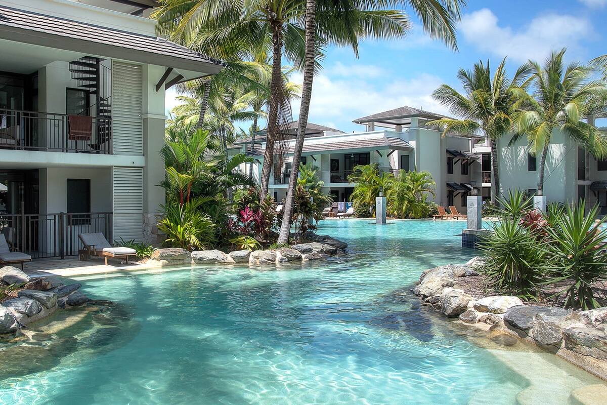 A resort with a clear pool, palm trees, and a two-story building with balconies.