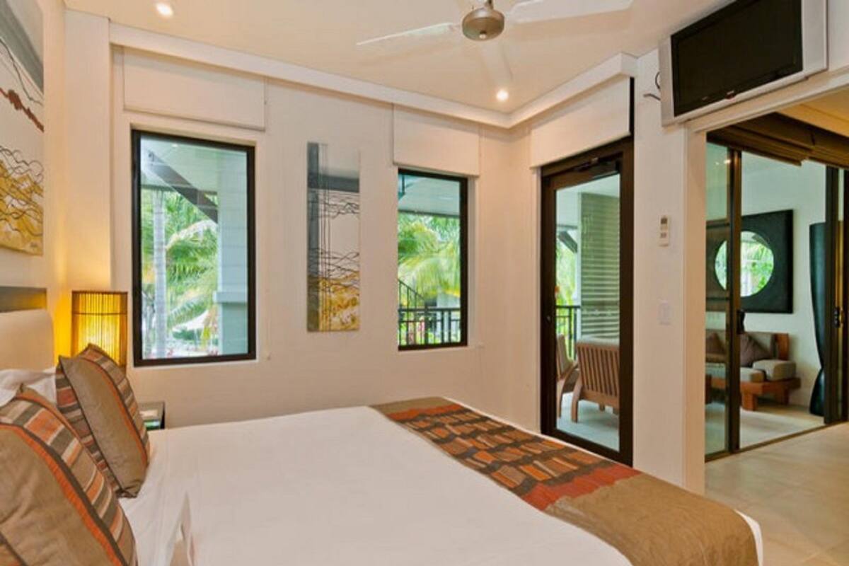 A modern hotel room with a large bed, a ceiling fan, and a balcony with a view of greenery.