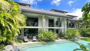 Un edificio de dos pisos con piscina y abundante vegetación.