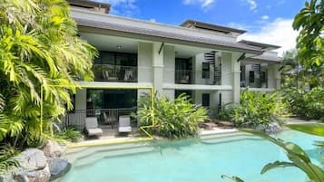 A two-story building with a pool and lush greenery.