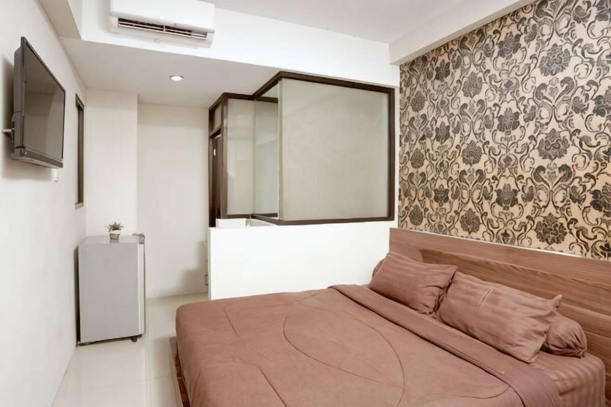 A bedroom with a bed, a TV, a small table, and a mirror.
