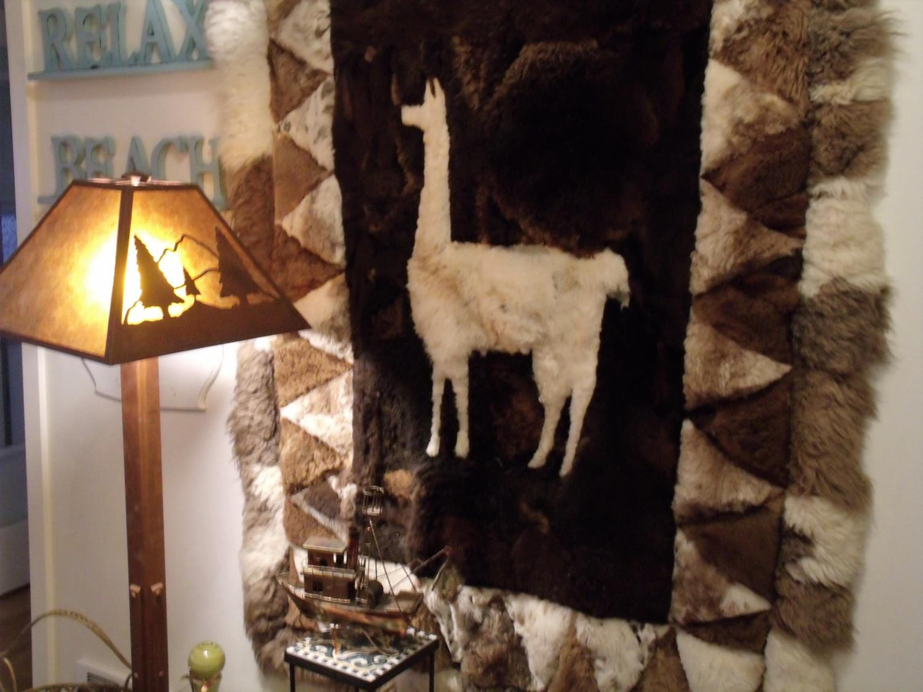 A room with a lamp, a wall hanging of a llama, and a ship model.