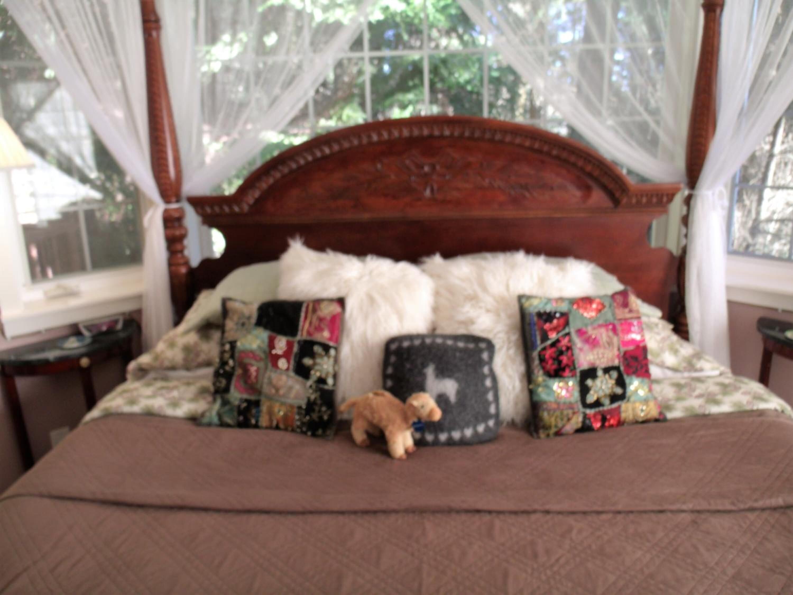 Una cama con colcha marrón, almohadas decorativas y un oso de peluche.