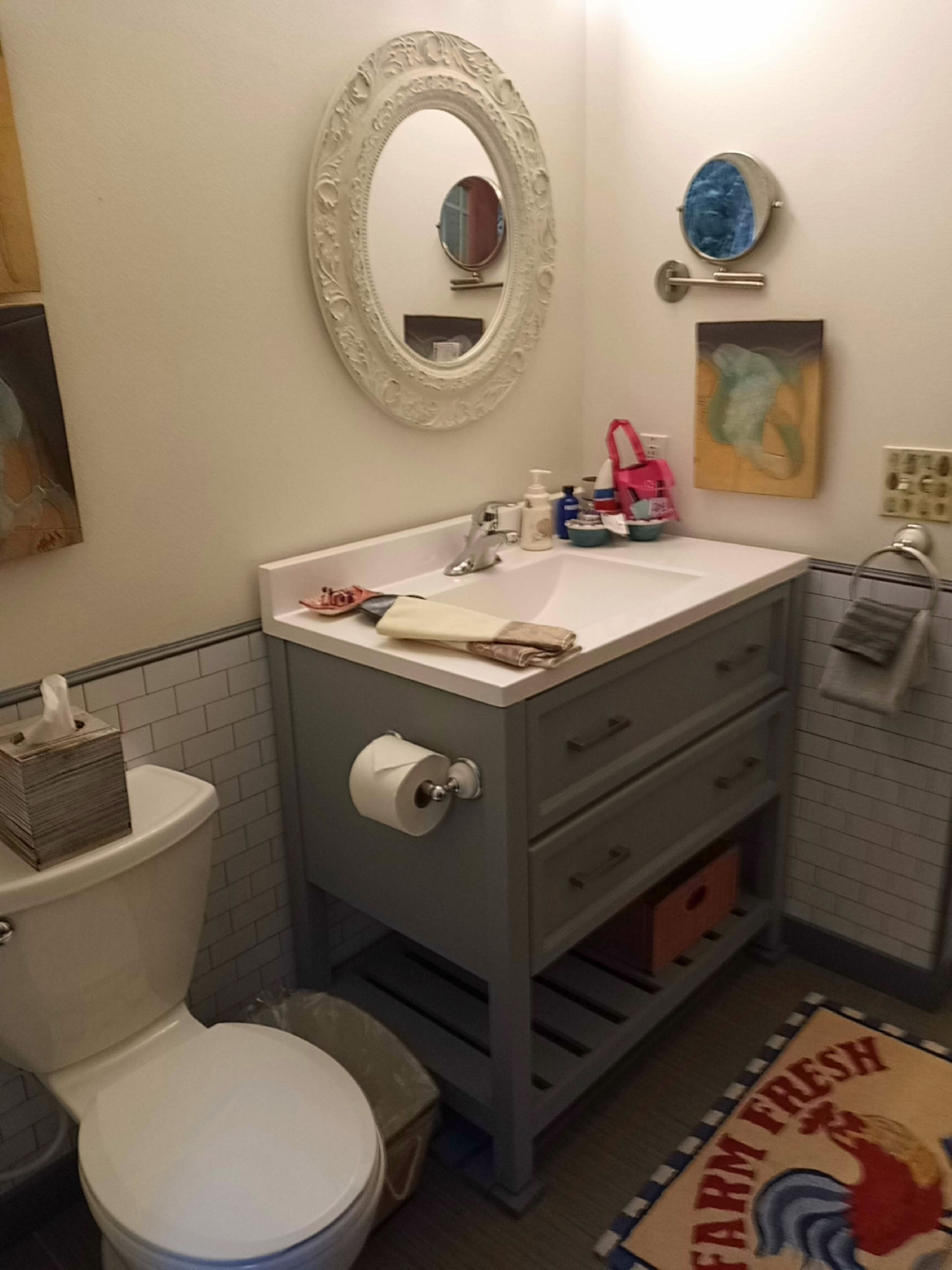 A bathroom with a toilet, sink, and mirror. There is a towel rack and a trash can.