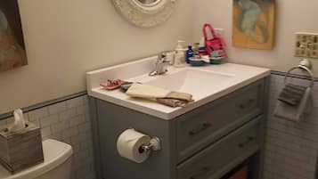 A bathroom with a toilet, sink, and mirror. There is a towel rack and a trash can.