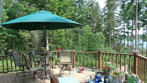 A wooden deck with wicker furniture, a table with a glass top, and potted plants.
