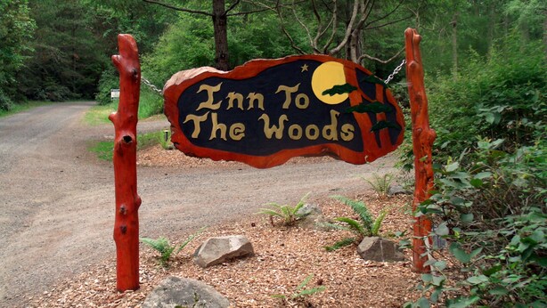 A rustic wooden sign with the text "Inn To The Woods" and a moon and stars design.