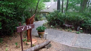 A wooden sign with "IN" written on it, a potted plant, and a pathway leading to a building.