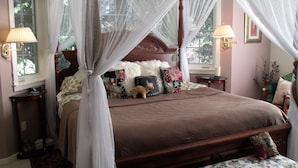 A four-poster canopy bed with a brown bedspread, multiple decorative pillows, and a floral-patterned bench at the foot of the bed.