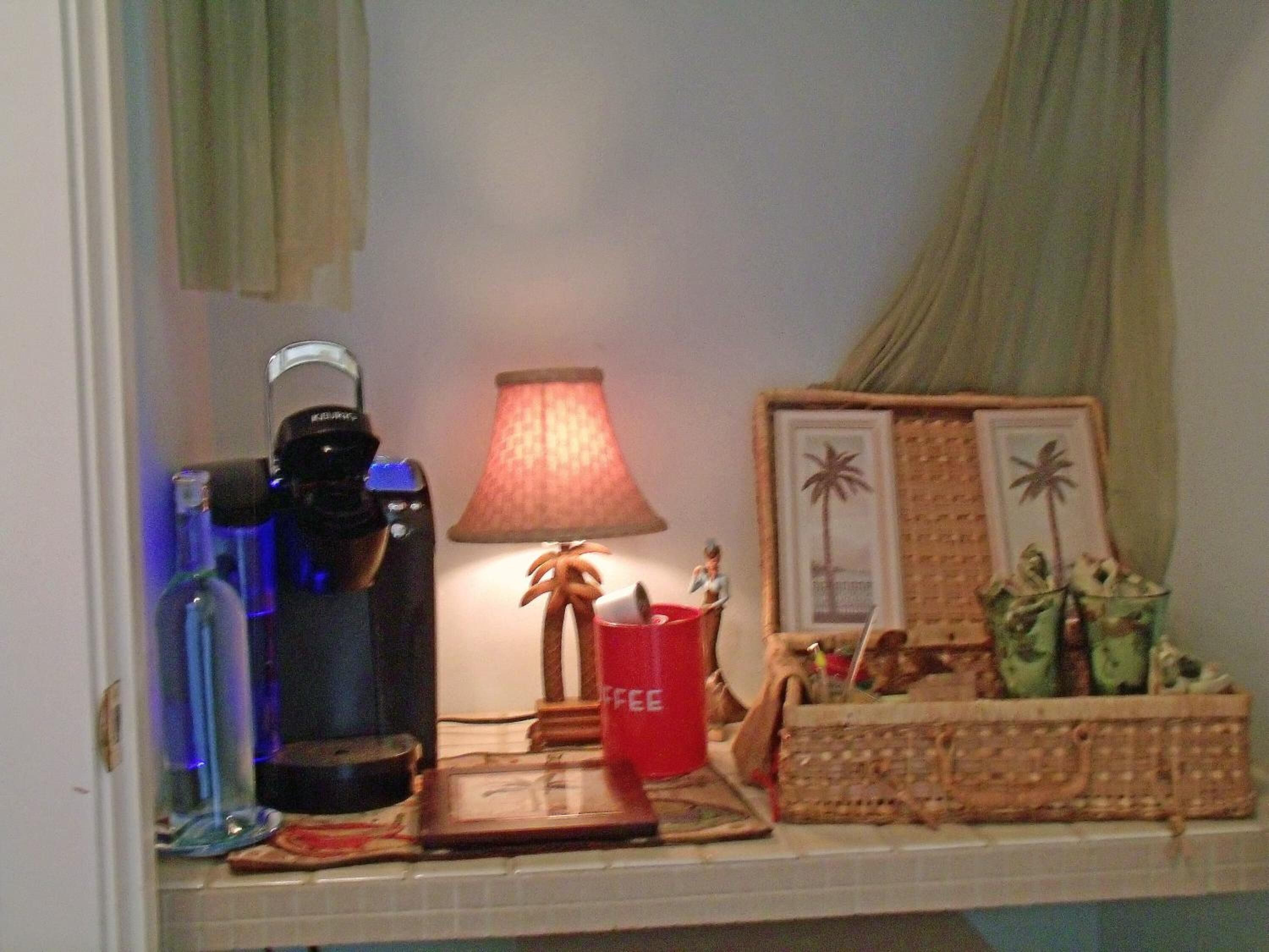 A kitchen counter with a coffee maker, a red cup, a small figurine, and a framed picture of palm trees.
