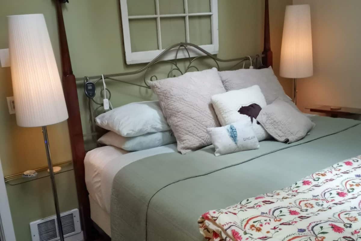 A bed with a green bedspread, multiple pillows, and two bedside lamps.