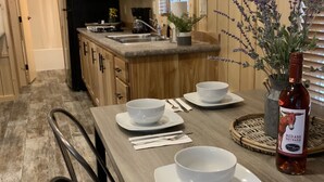 Een moderne keuken met houten kastjes, een zwarte koelkast, een spoelbak en een eethoek met witte borden, kommen en bestek.