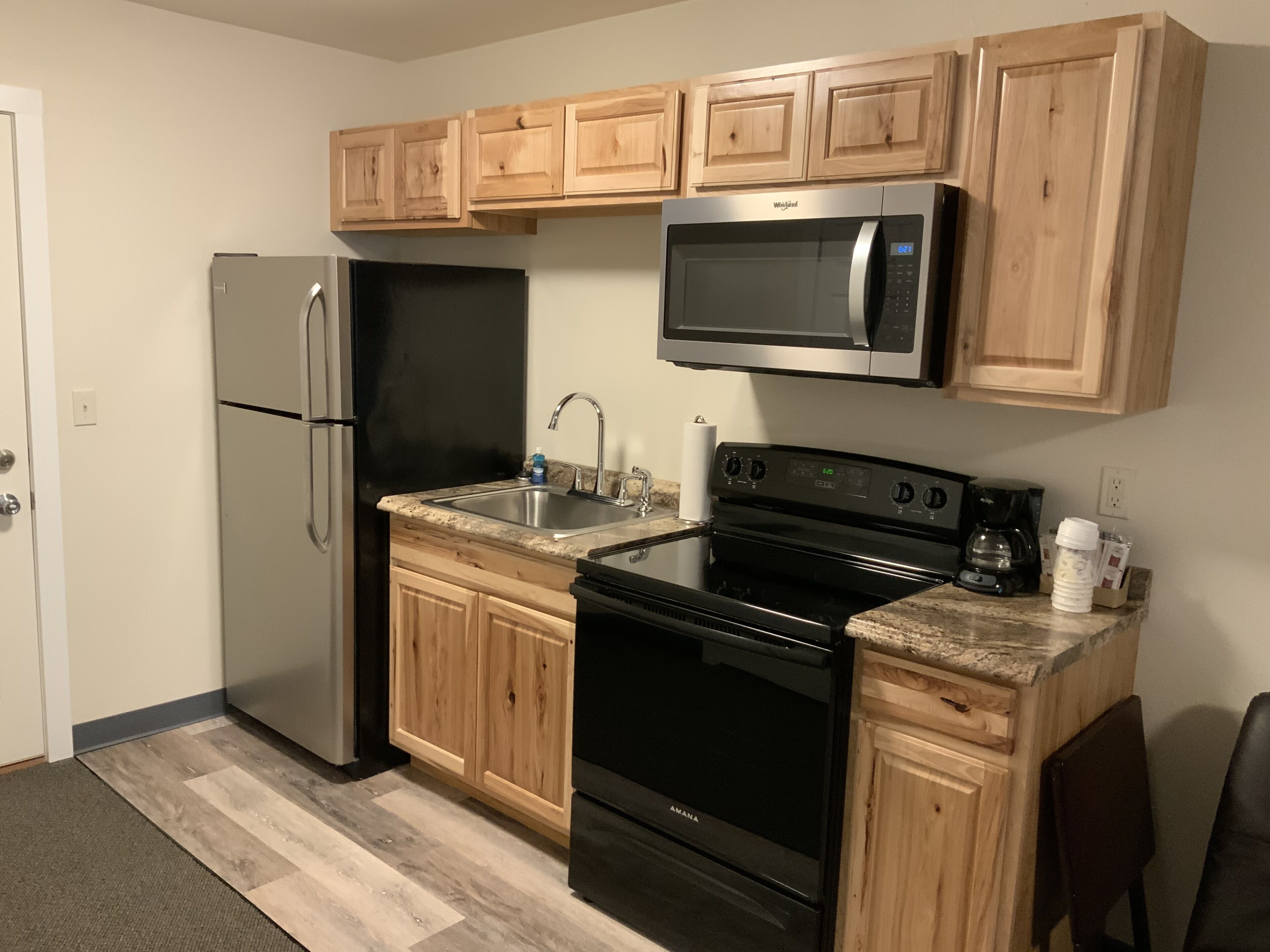 Una cocina con armarios de madera, un refrigerador de acero inoxidable, un microondas, una estufa y un lavamanos.