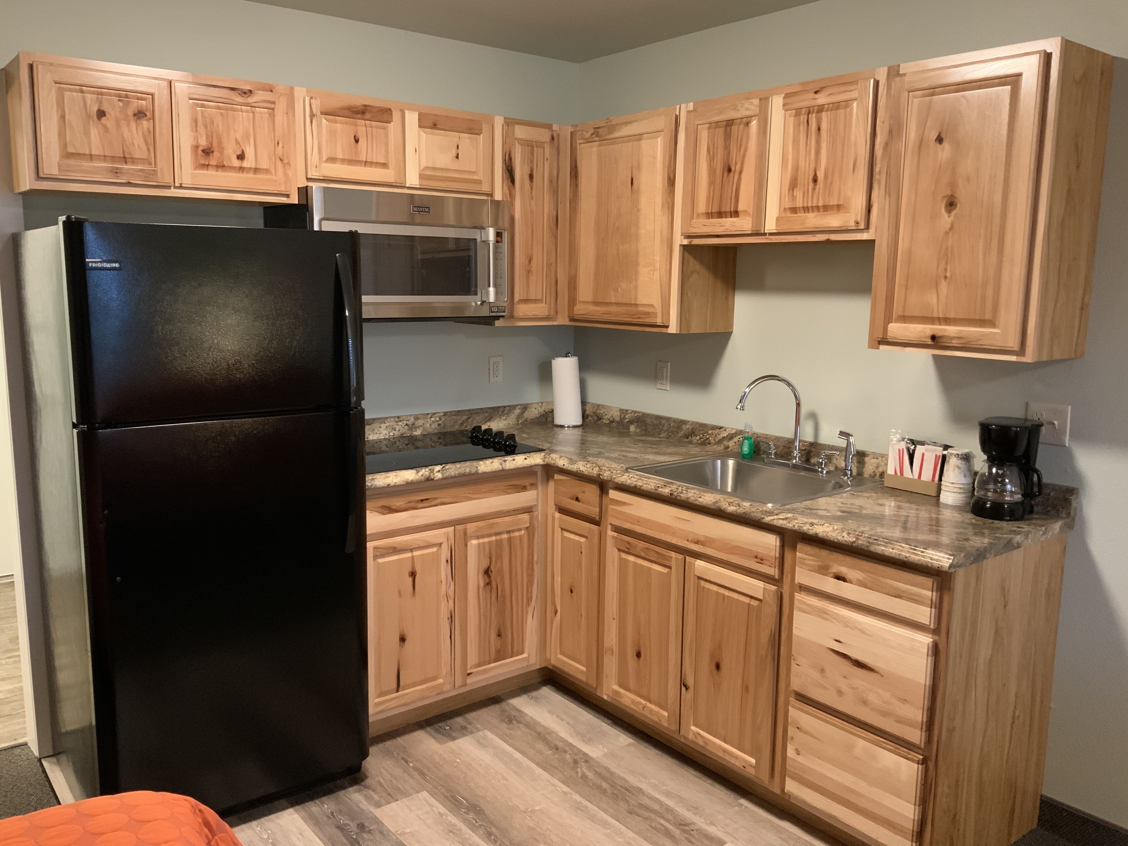 Uma cozinha com armários de madeira, geladeira preta, micro-ondas, pia e máquina de café.