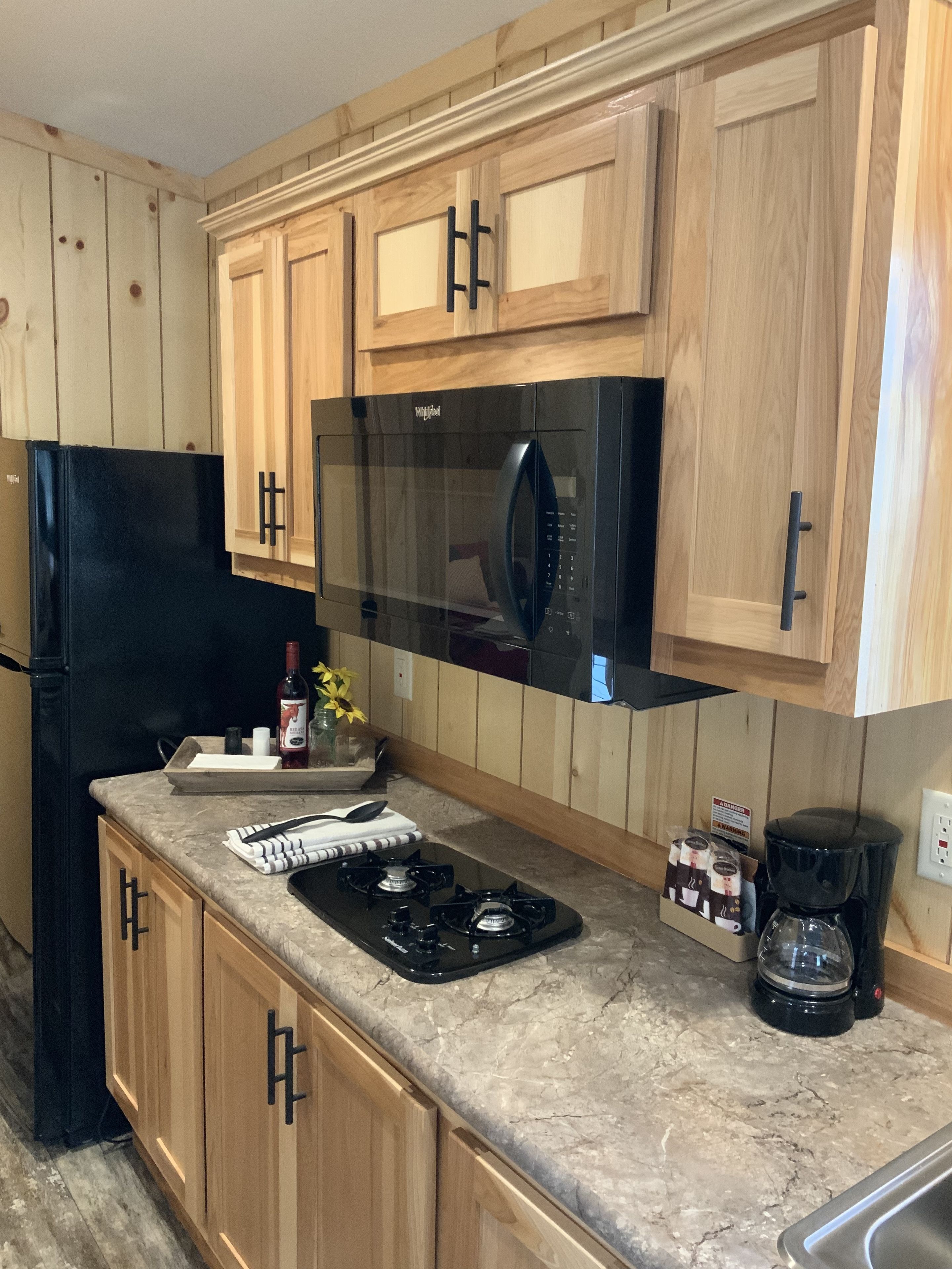 A kitchen with wooden cabinets, a black refrigerator, a microwave, a gas stove, and a coffee maker.