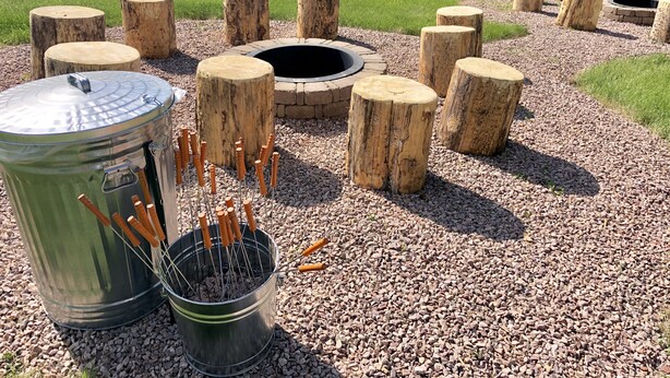 Een rustieke buitenplaats met een metalen barbecue, houten krukken en een vuurkuil.