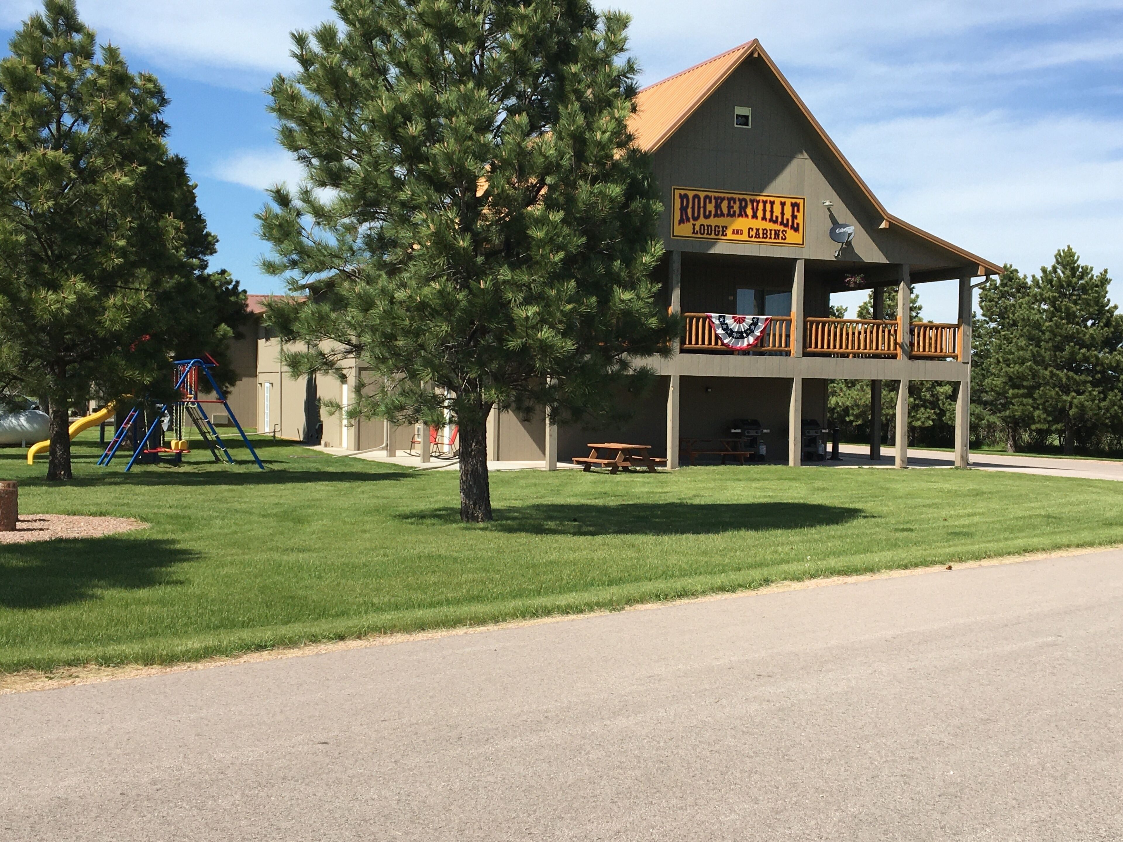 A lodge with a sign reading "Rockerville Lodge and Cabins" featuring a covered porch and picnic tables.