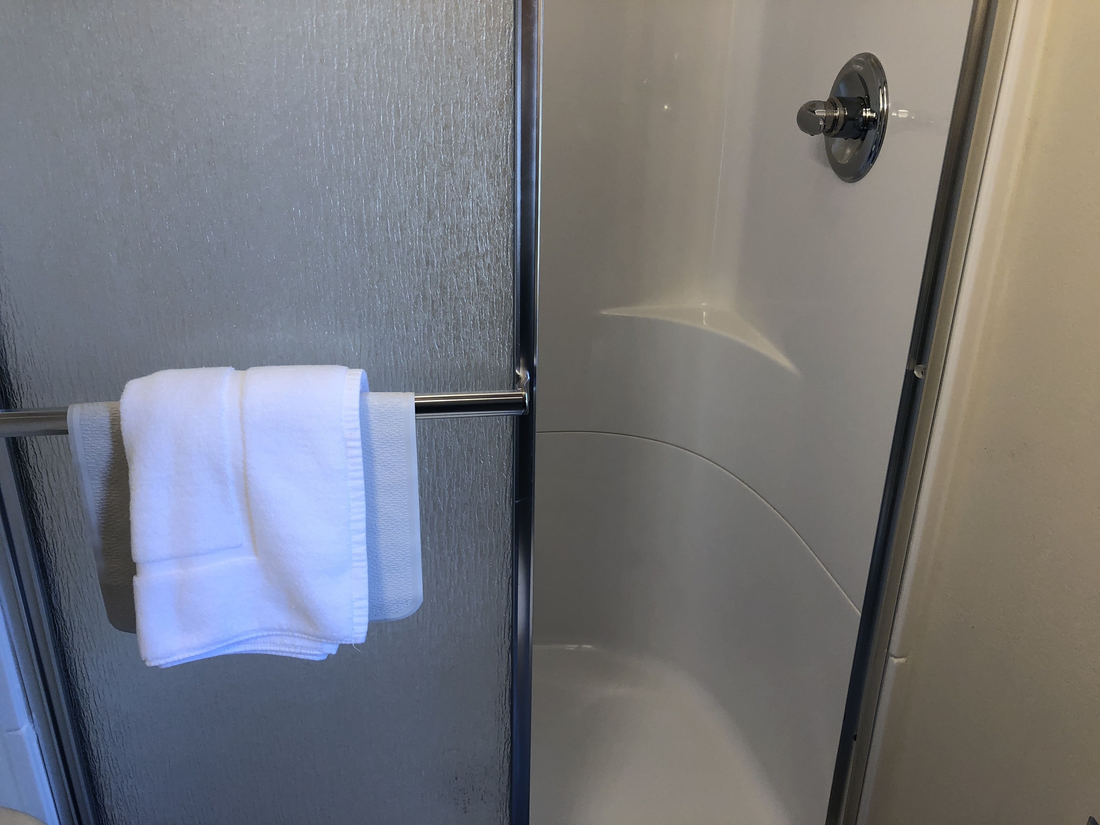 Un box de ducha con paredes de vidrio y un perchero con una toalla doblada.