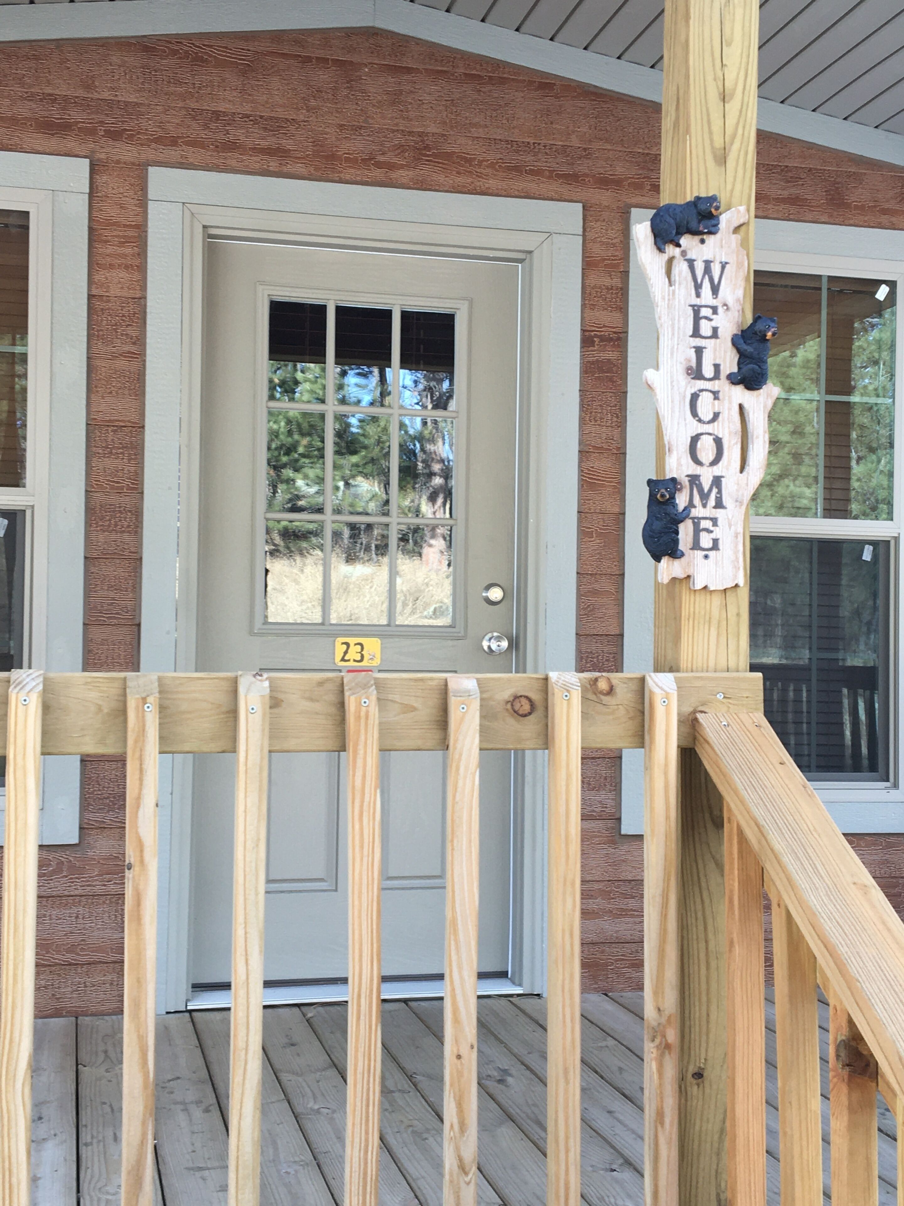 A wooden deck with a welcome sign featuring bears, a door with a number 23 sign, and a brick house facade.