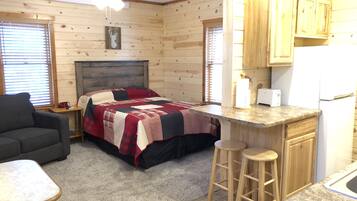 A cozy cabin with a bed, a small kitchenette, a dining area, and a ceiling fan.