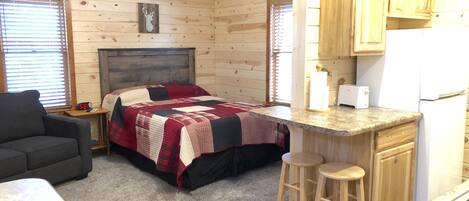 A cozy cabin with a bed, a small kitchenette, a dining area, and a ceiling fan.