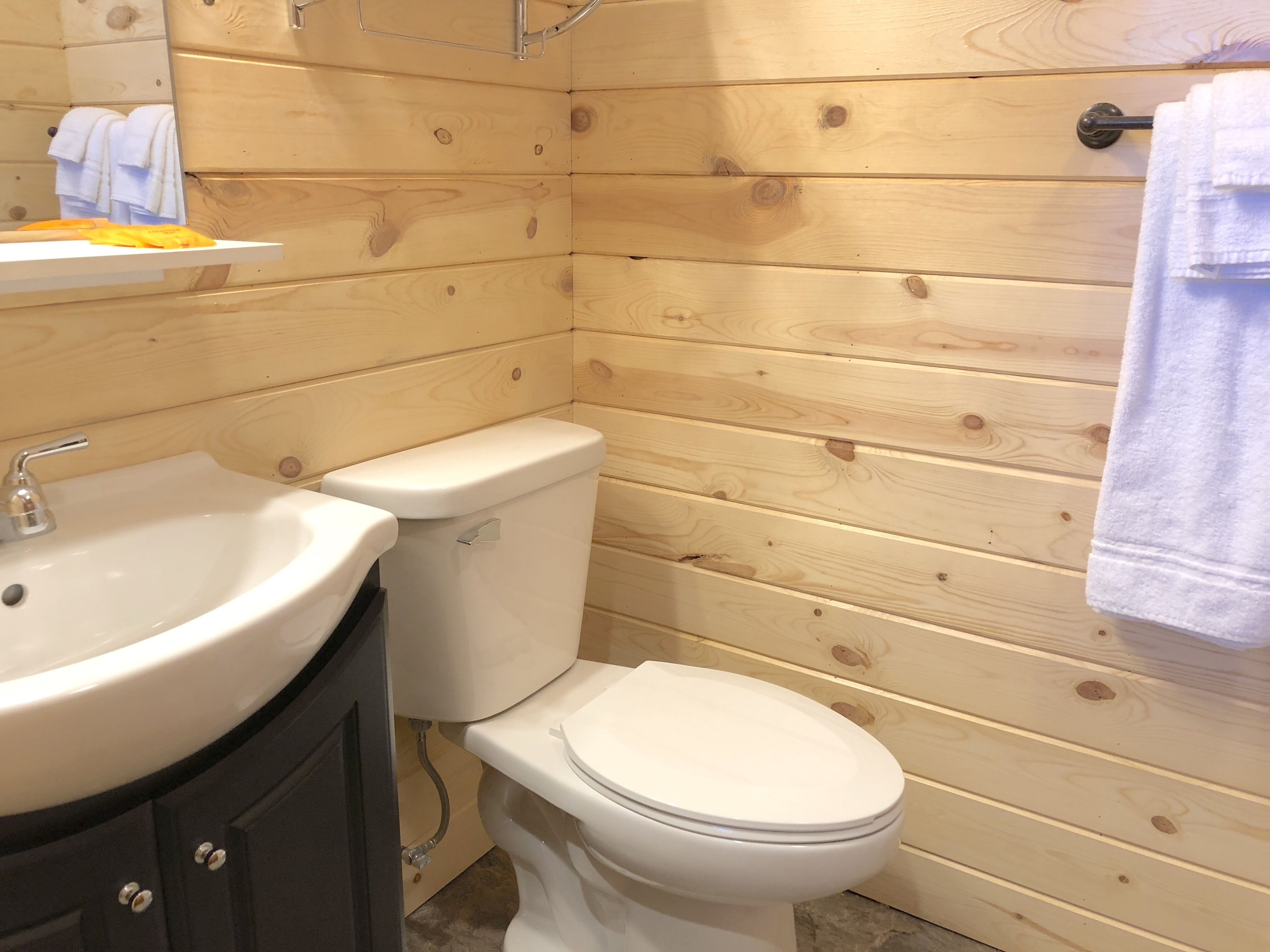 Une salle de bain aux murs lambrissés, avec un lavabo, des toilettes et un porte-serviettes, le tout de couleur blanche.
