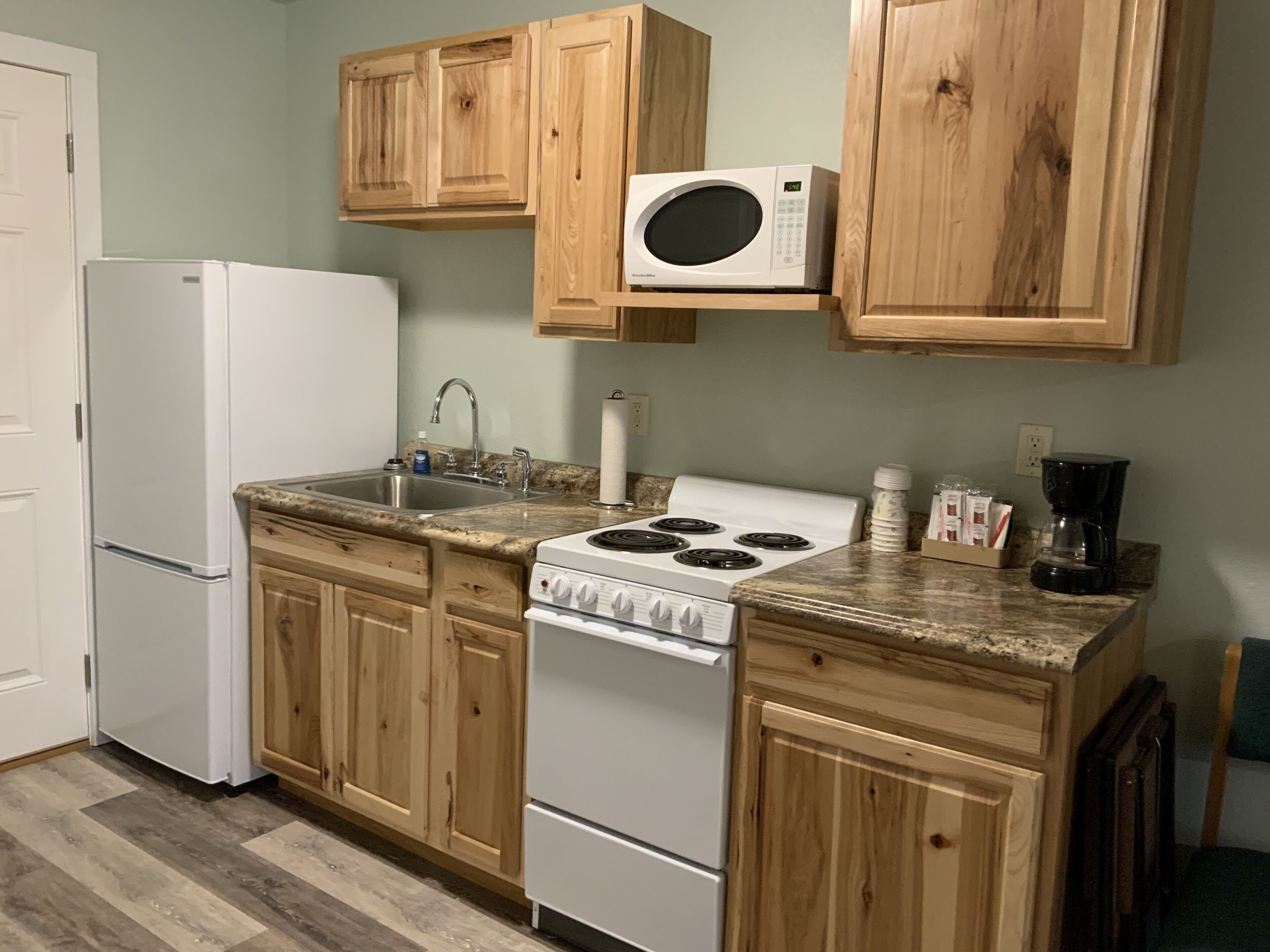 Una cocina con gabinetes de madera, un refrigerador blanco, estufa, microondas y cafetera.