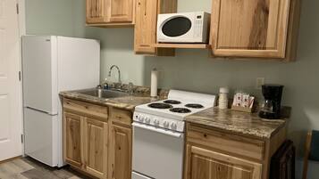 A kitchen with wooden cabinets, a white refrigerator, a stove, a microwave, and a coffee maker.