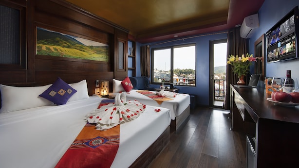 A hotel room with two beds, a large window with a city view, a desk with a computer, and a TV mounted on the wall. - Sapa Sweet Time Hotel (Sa Pa)