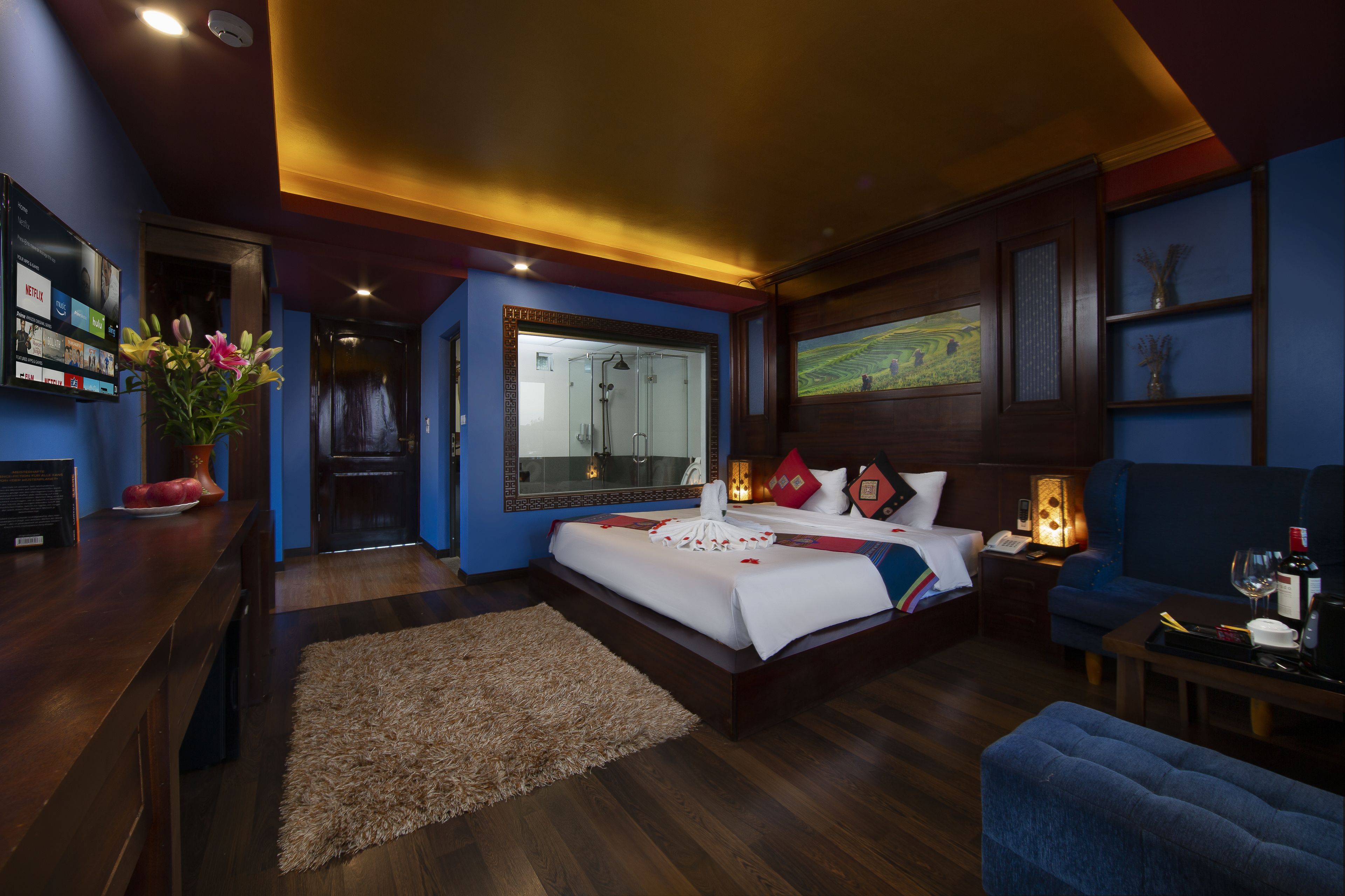 A modern hotel room with a large bed, a sitting area, a shower, and a TV on the wall.