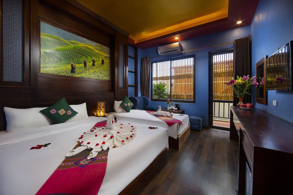 Habitación de hotel con dos camas, un ventanal con persianas, un aire acondicionado instalado en la pared y un cuadro de un paisaje.
