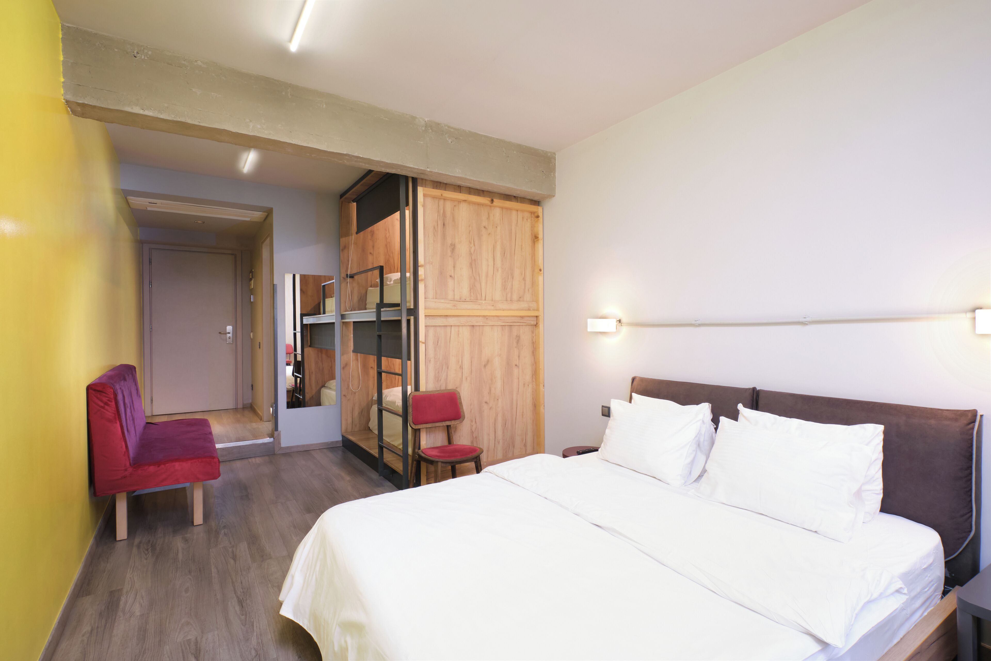 Ein Schlafzimmer mit einem Bett, einem roten Sessel, einem Holzschrank und einer Tür zu einem anderen Raum.