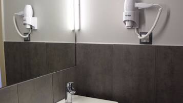 Une salle de bain avec un lavabo blanc, un miroir et deux sèche-cheveux fixés au mur.