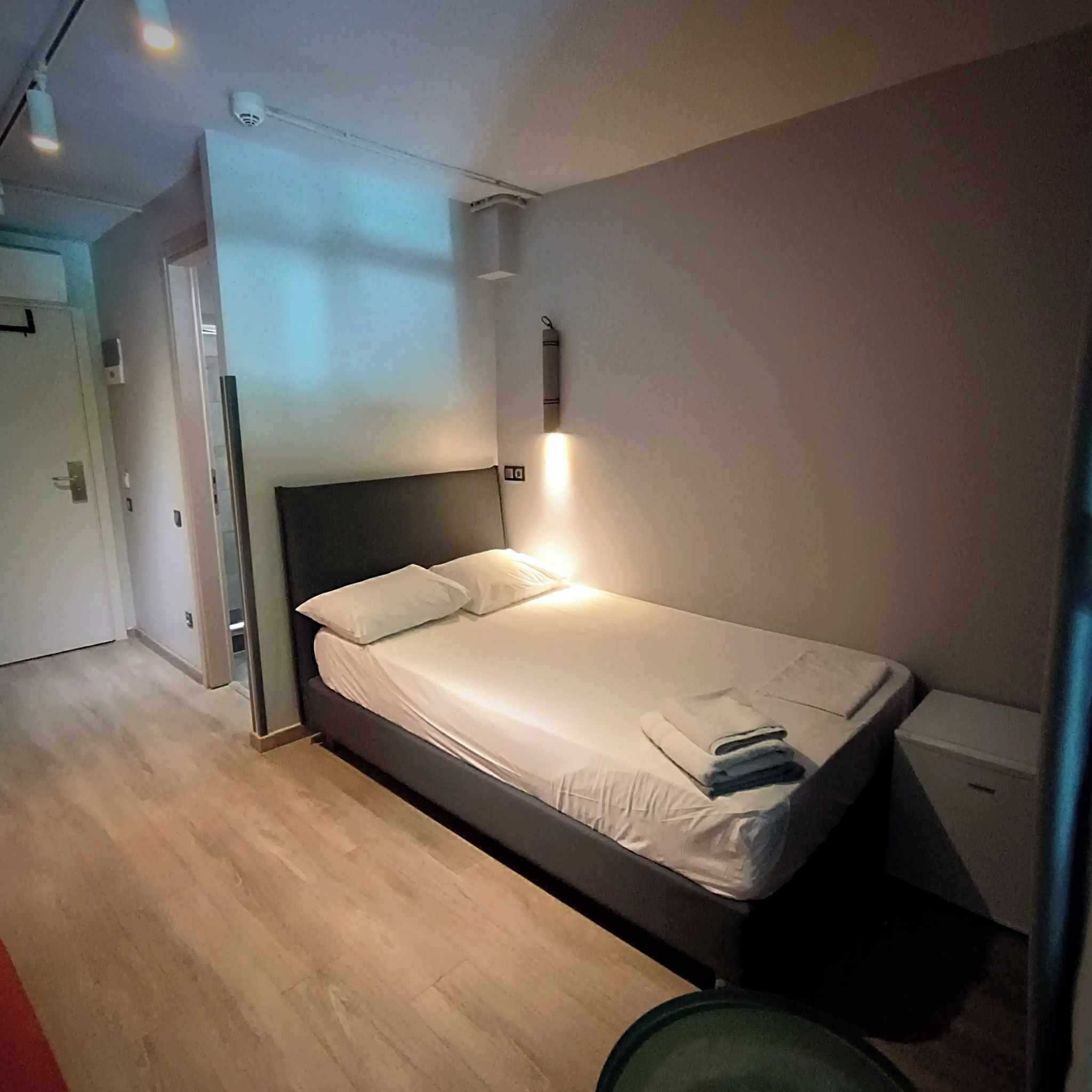 A single bed with a headboard, a bedside table, and a wall-mounted light.