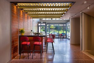 Un área de bar moderna con taburetes rojos, una pared de ladrillo y vistas al exterior a través de amplios ventanales.