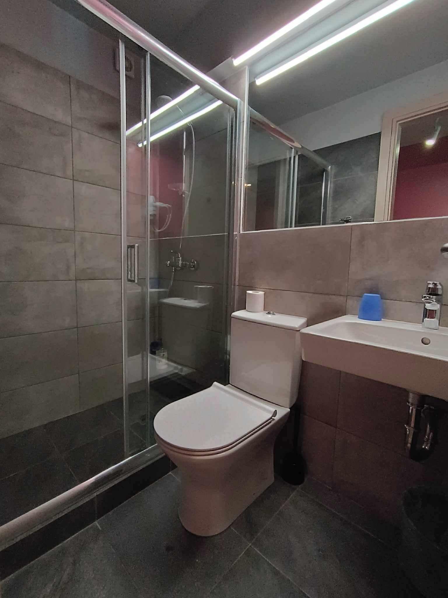 Une salle de bain moderne avec une douche à parois de verre, des toilettes et un lavabo surmonté d’un miroir.