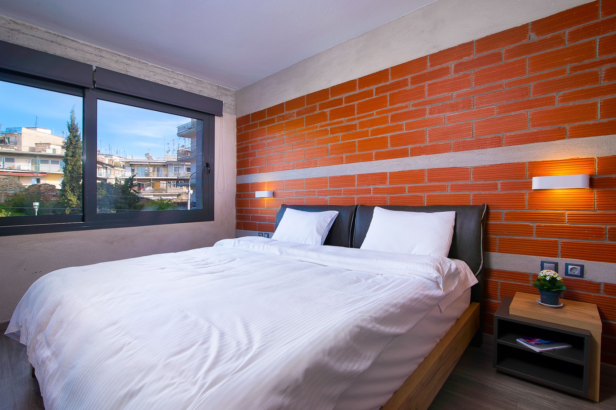 Ein Hotelzimmer mit einem großen Bett, einer Ziegelwand und einem Fenster mit Blick auf eine Stadtansicht.