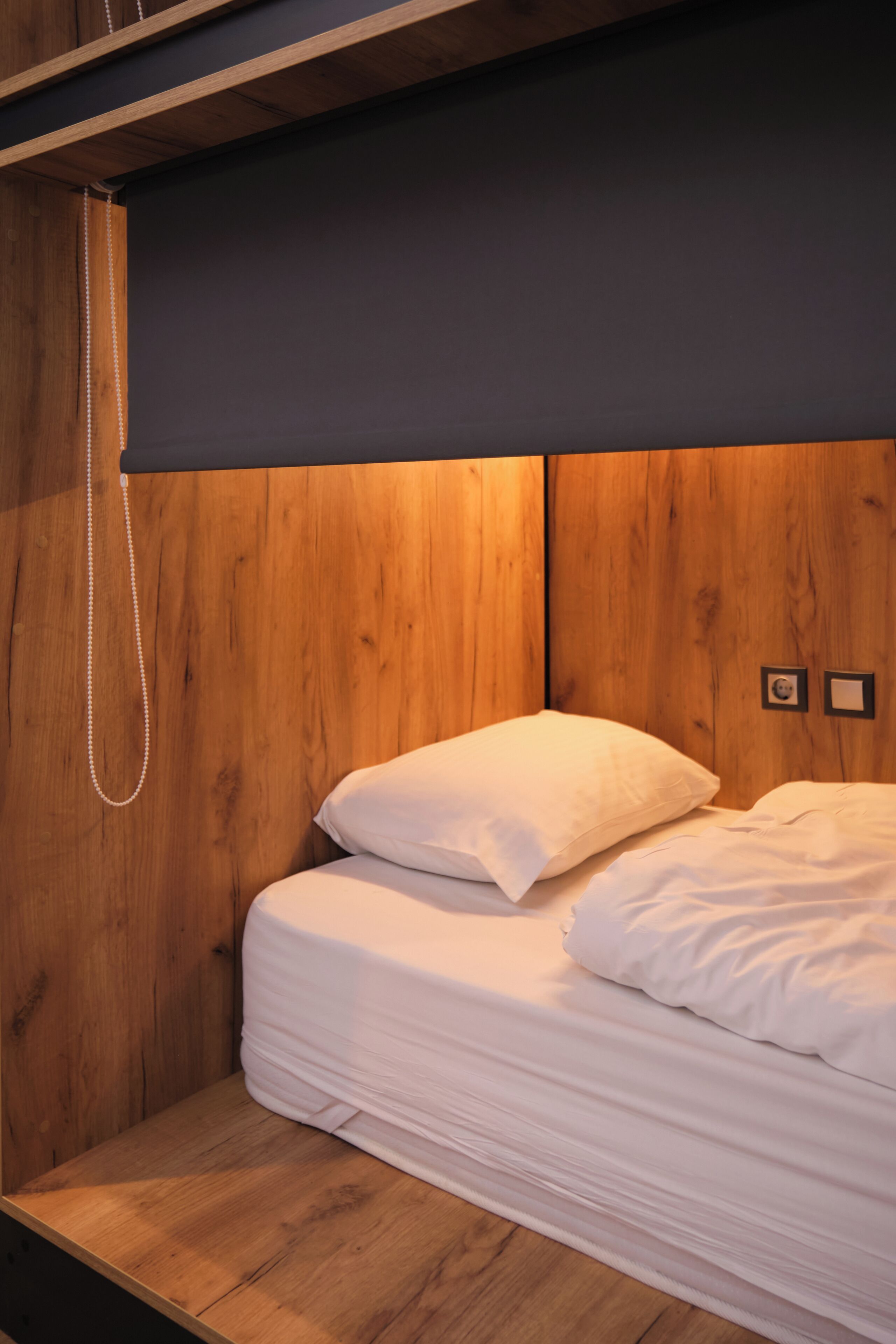 A wooden room with a bed, a hanging light fixture, and a small wall-mounted clock.