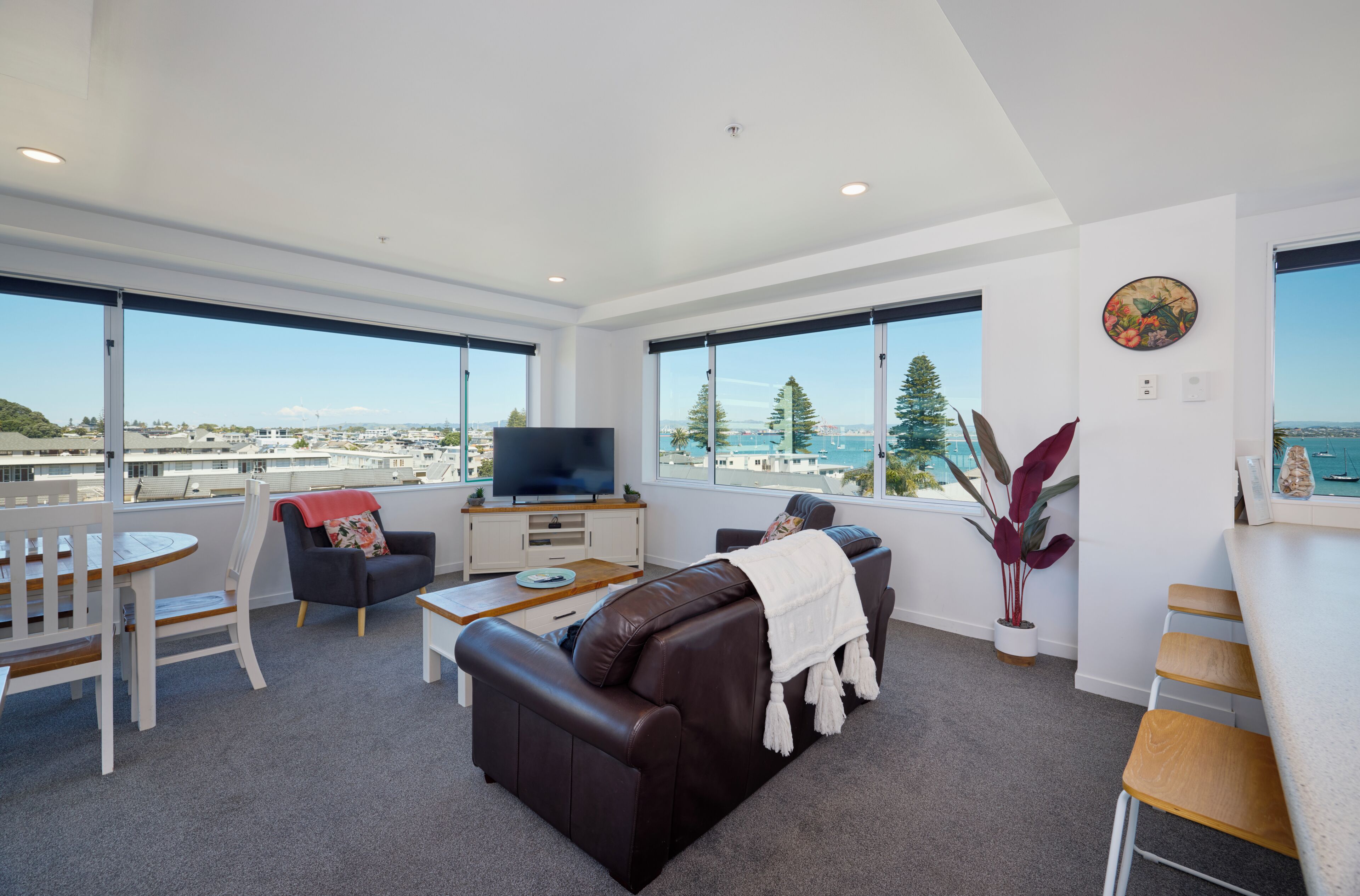 A modern living room with a large window, a sofa, a TV, and a dining area.