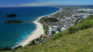 A coastal town with a beach, buildings, and a hill with vegetation. - The Beaumont Apartments (Tauranga)