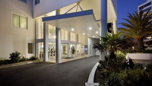 A modern hotel entrance with a covered walkway, large windows, and a palm tree in the foreground. - The Beaumont Apartments (Tauranga)